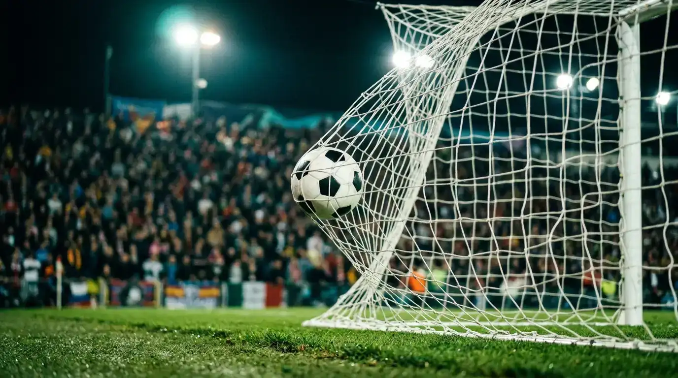 Nahaufnahme eines Fussballs im Tornetz bei Flutlicht, im Hintergrund unscharfe gefüllte Ränge